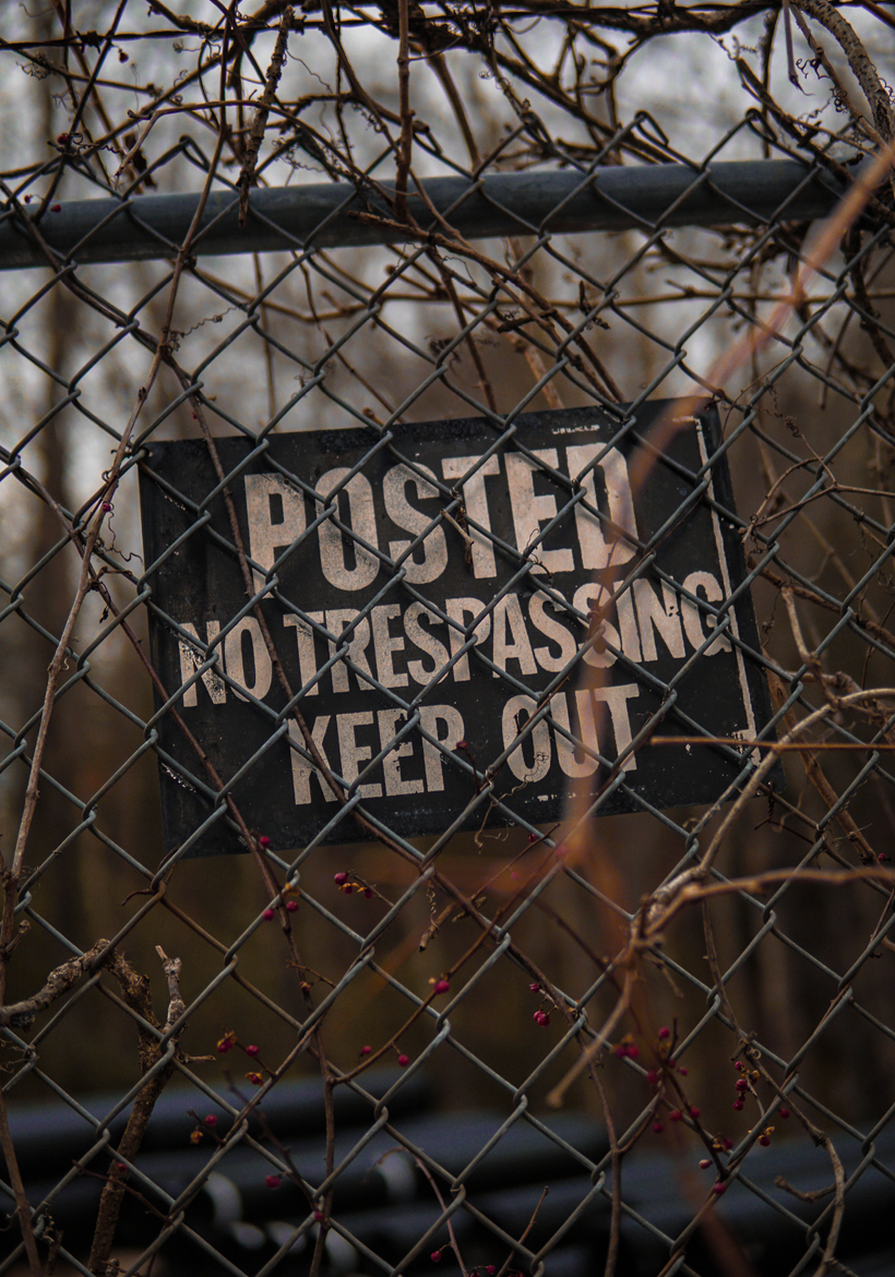 no trespassing keep out posted sign behind metal fence